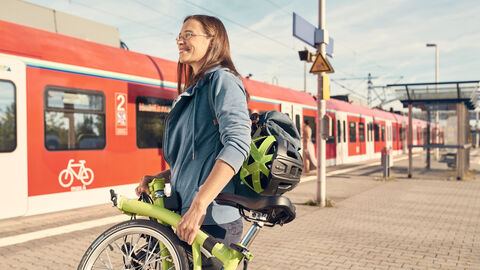Pendlerin mit Klapprad an S-Bahn Station Frau steht mit Klapprad vor einer S-Bahn