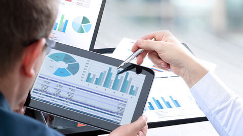 Eine Person zeigt auf Diagramme die auf dem Bildschirm eines Tablets zu sehen sind