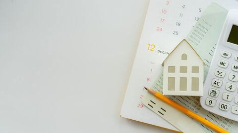 Taschenrechner, Bleistift und Miniatur eines Hauses auf dem Schreibtisch Taschenrechner, Bleistift und Miniatur eines Hauses auf dem Schreibtisch