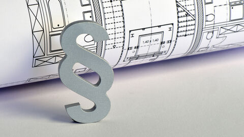 Ein dreidimensionaler Paragraph steht vor einem Bauplan