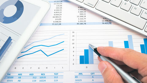 Hand mit Kugelschreiber über Blätter mit Diagrammen