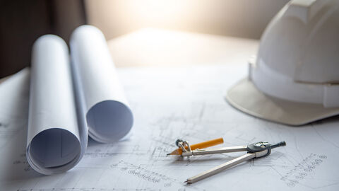 Architekturpläne und Bauhelm liegen auf einem Tisch