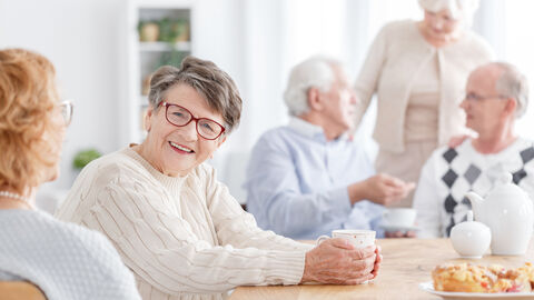 Senioren sitzen zusammen, ältere Dame lächelt in Kamera