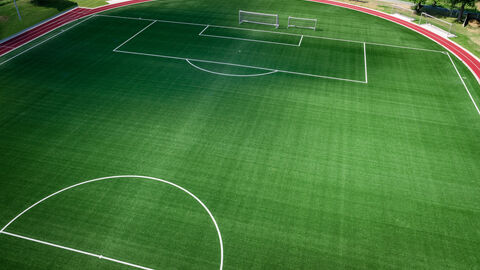 Blick aus Vogelperspektive auf einen Fußballplatz mit Kunstrasen und Tartanbahn