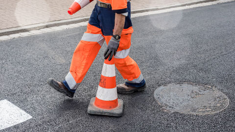 Bauarbeiter trägt Verkehrspylonen auf sanierter Straße Bauarbeiter trägt Verkehrspylonen auf sanierter Straße