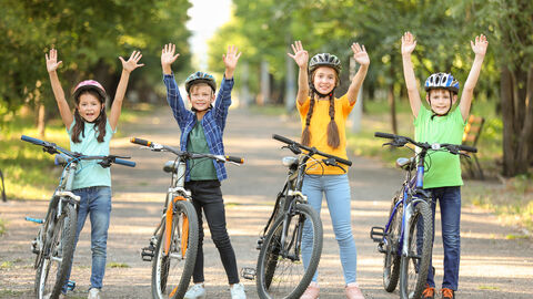 Kinder mit Fahrrädern strecken die Arme nach oben