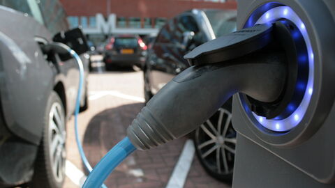 Nahaufnahme einer E-Ladestation mit E-Auto im Hintergrund