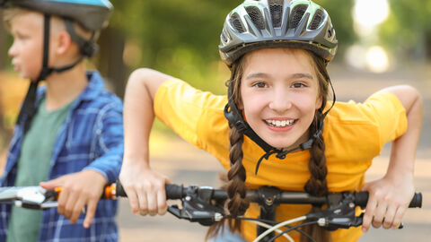 Ein lachendes Mädchen mit Helm auf einem Fahrrad schaut in die Kamera
