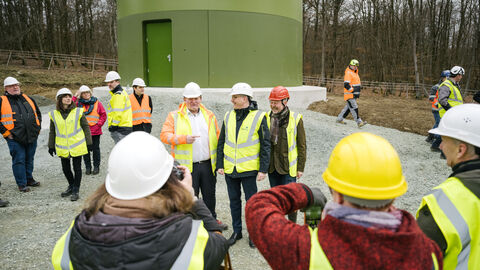 Energieminister Al-Wazir mit anderen Leuten in gelber Jacke und mit Helm bei der Baustellenbesichtigung vor einem Windrad.