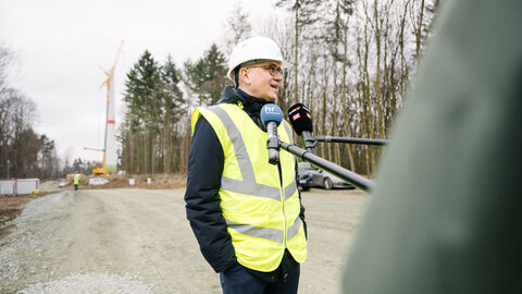 Besuch der Baustelle des Windparks Leun-Löhnberg Energieminister Al-Wazir in gelber Jacke und mit Helm und Mikrofonen in einer Interviewsituation mit der Presse bei der Baustellenbesichtigung vor einem Windrad..