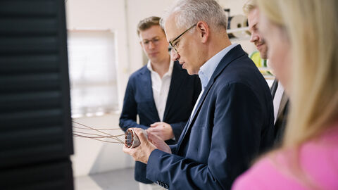 Al-Wazir hält ein Metallteil in Händen und begutachtet es, um ihn weitere Personen.