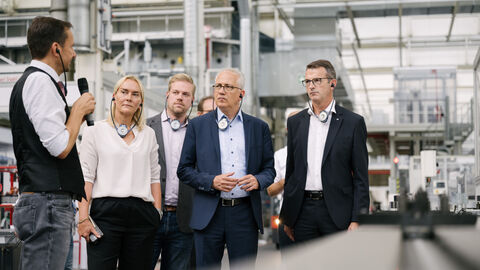 Eine Gruppe um Wirtschaftsminister Al-Wazir steht zusammen in einer Werkshalle. Eine weitere Person mit Mikrofon erklärt.