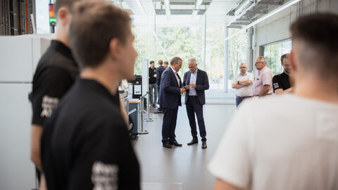 Im Vordergrund mehrere Personen verschwommen, im Hintergrund Wirtschaftsminister Al-Wazir im Gespräch.