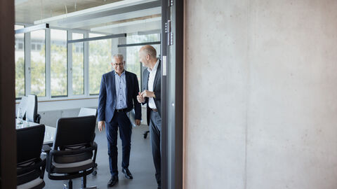 Blick in einen Meeting-Raum. Dort stehen Wirtschaftsminister Al-Wazir und ein weiterer Mann ins Gespräch vertieft.