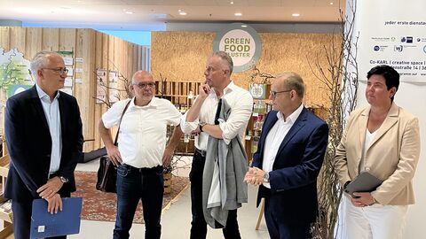 Vier Männer und eine Frau stehen vor einem Verkaufsstand, auf dem Green Food steht