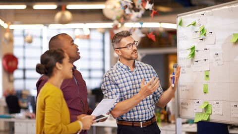 Eine Frau und zwei Männer stehen an einem Whiteboard