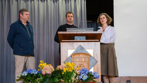 Team des Projektes Mikro-Genossenschaften und dreifache Innenentwicklung Drei Personen stehen an einem Pult auf einer Bühne