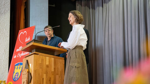 Drei Personen stehen an einem Pult auf einer Bühne