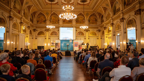 Blick in einen großen Raum. Mehrere bestulte Publikumsreihen