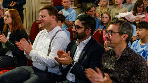 Applaus für die Siegerschulen Drei Männer sitzen auf Stühlen und klatschen