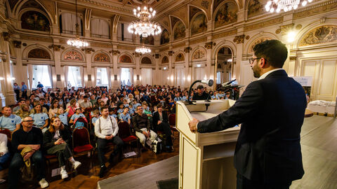 Blick in einen großen Sahl in dem mehrere Personen sitzen