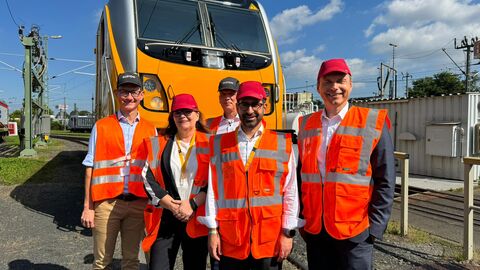 Mehrere Personen stehen mit orangenen Westen vor einem Zug