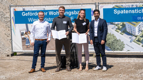 Vier Personen lachen in die Kamera. Zwei von Ihnen halten einen Förderbescheid.