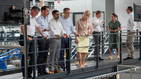 Mehrere Personen stehen auf einer Brücke in einer Industriehalle