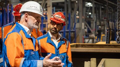 Zwei Männer mit Helmen und orangenen Jacken unterhalten sich 