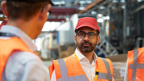 Ein Mann unterhält sich mit einem anderen Mann. Er trägt eine orangene Weste