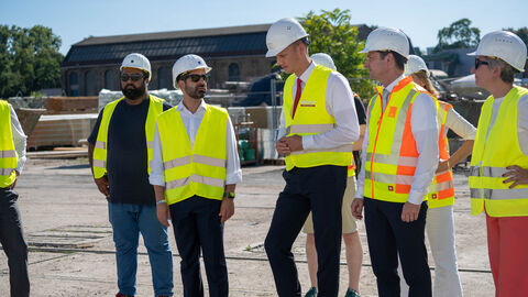 Mehrere Personen stehen mit gelben Warnwesten auf einer Baustelle