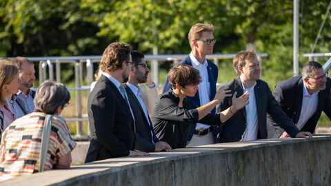 Mehrere Personen stehen an einer Mauer zu einem Klärbecken