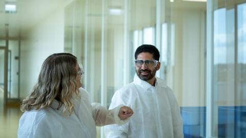 Ein Mann mit einer Laborbrille und weißen Kittel lässt sich etwas von einer Frau erklären