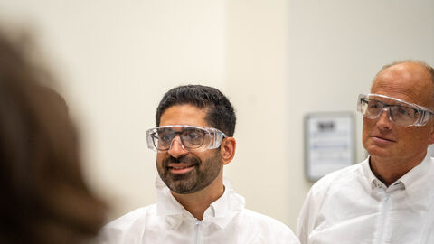 Ein Mann lacht in die Kamera. Er trägt eine Laborbrille und einen weißen Kittel