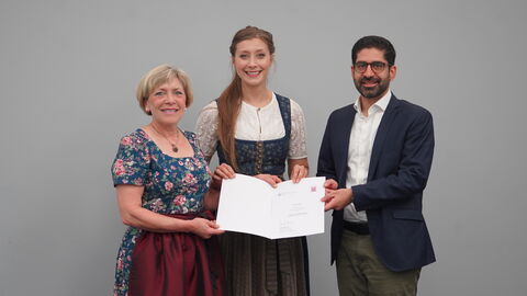 Zwei Frauen und ein Mann halten eine Urkunde