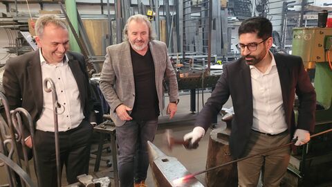 Drei Männer stehen in einer Metallmanufaktur