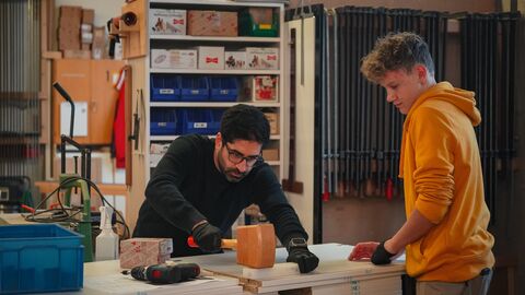 Ein Mann steht an einer Werkbank, ein anderer Mann steht dabei