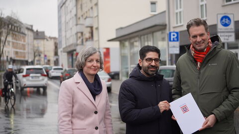 Bescheidübergabe in Kassel Drei Personen stehen an einer Straße