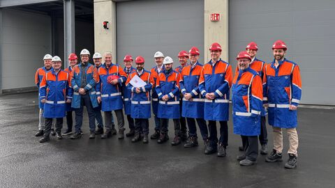 Mehrere Männer in orange-blauen Sicherheitsanzügen stehen vor einem Tor