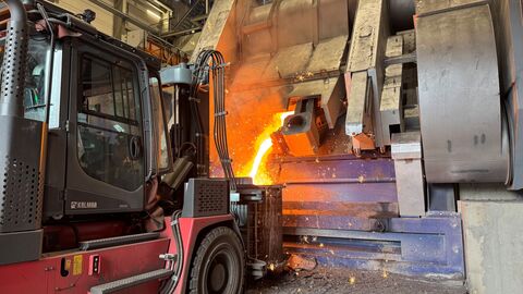 Ein Bagger steht vor einem Metallhochofen aus dem flüssiges Metall fließt