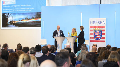 Nahmobilitätskongress Drei Personen stehen auf einer Bühne in einem Kongressaal