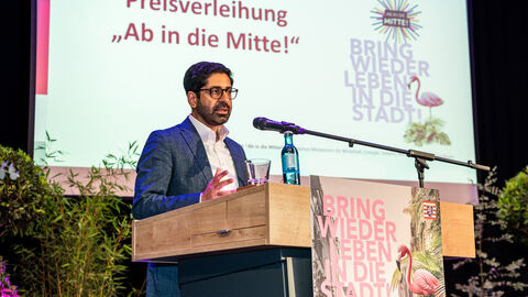 Ein Mann steht auf einer Bühne und spricht in ein Mikro