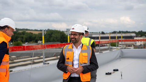Besuch der Baustelle der neuen Werkstatt der Hessischen Landesbahn Ein Mann steht mit Helm und Warnweste auf einem Hallendach
