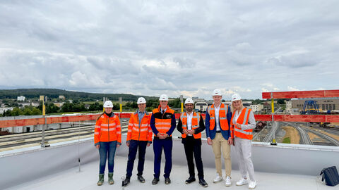 Besuch der Baustelle der neuen Werkstatt der Hessischen Landesbahn Mehrere Personen in orangenen Warnwesten stehen auf dem Dach einer Halle