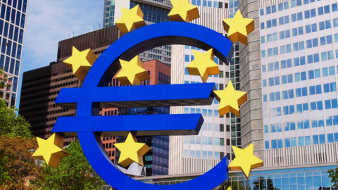 Europäische Zentralbank Ein großes Euro-Zeichen in Blau mit Sternen drum herum. Im Hintergrund Hochhäuser