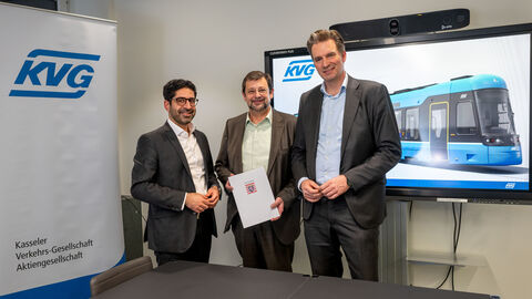 Drei Männer in Anzügen lachen in die Kamera. Einer hält einen Förderbescheid in der Hand