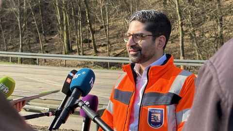 Ein Mann in einer orangenen Warnweste spricht in mehrere Mikrofone